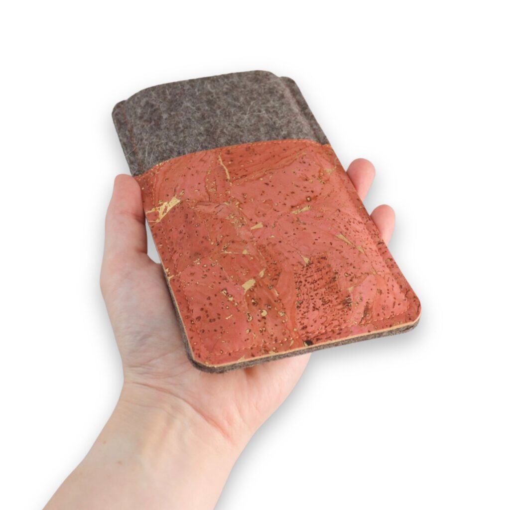 Handgemachte Handytasche aus Filz und korallfarbenem Kork mit Goldmuster, in einer Hand gehalten