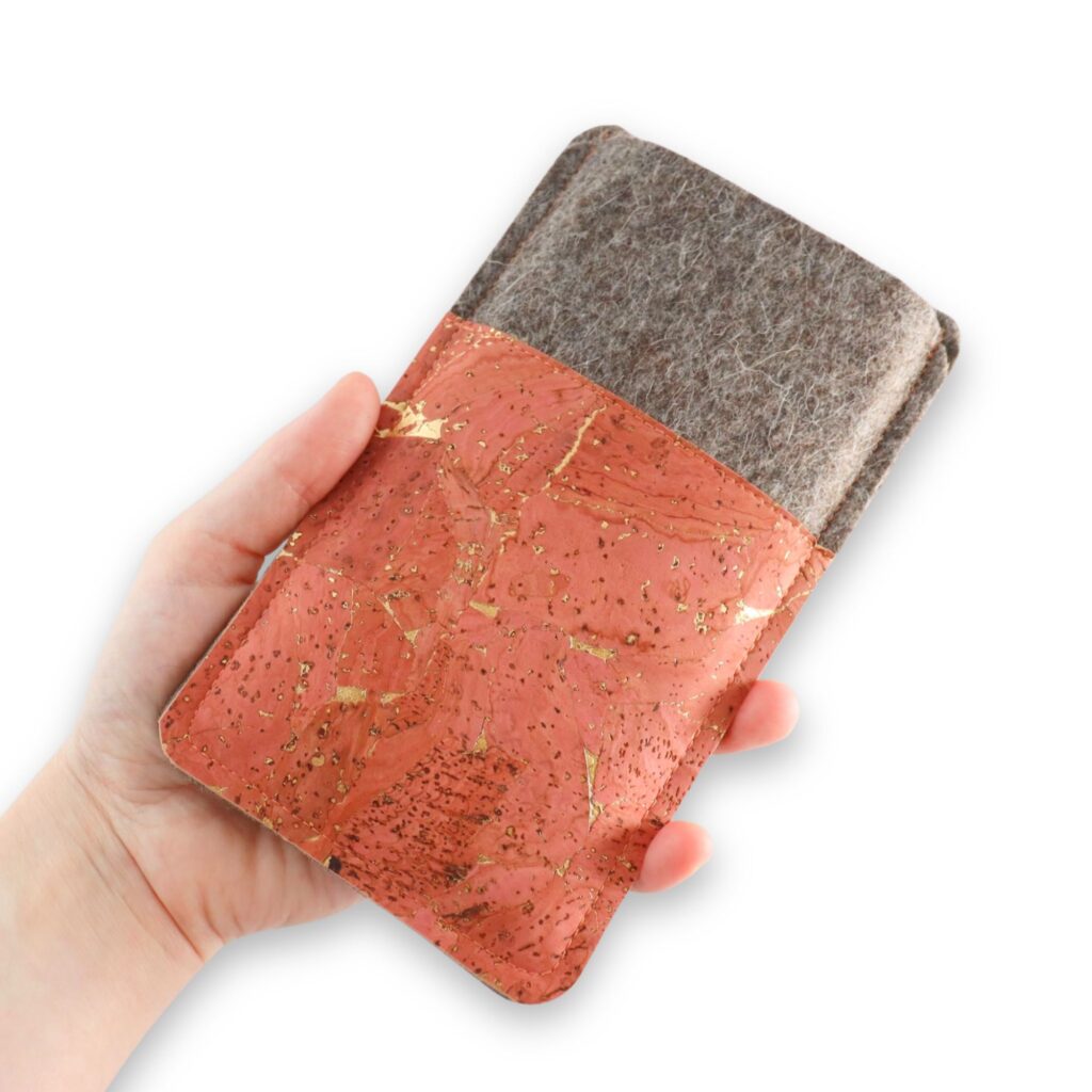 Handgemachte Handytasche aus Filz und korallfarbenem Kork mit Goldmuster, in einer Hand gehalten