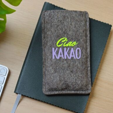Handytasche aus grauem Filz mit Print "Ciao Kakao", auf einem Notizbuch liegend