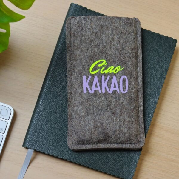 Handytasche aus grauem Filz mit Print "Ciao Kakao", auf einem Notizbuch liegend