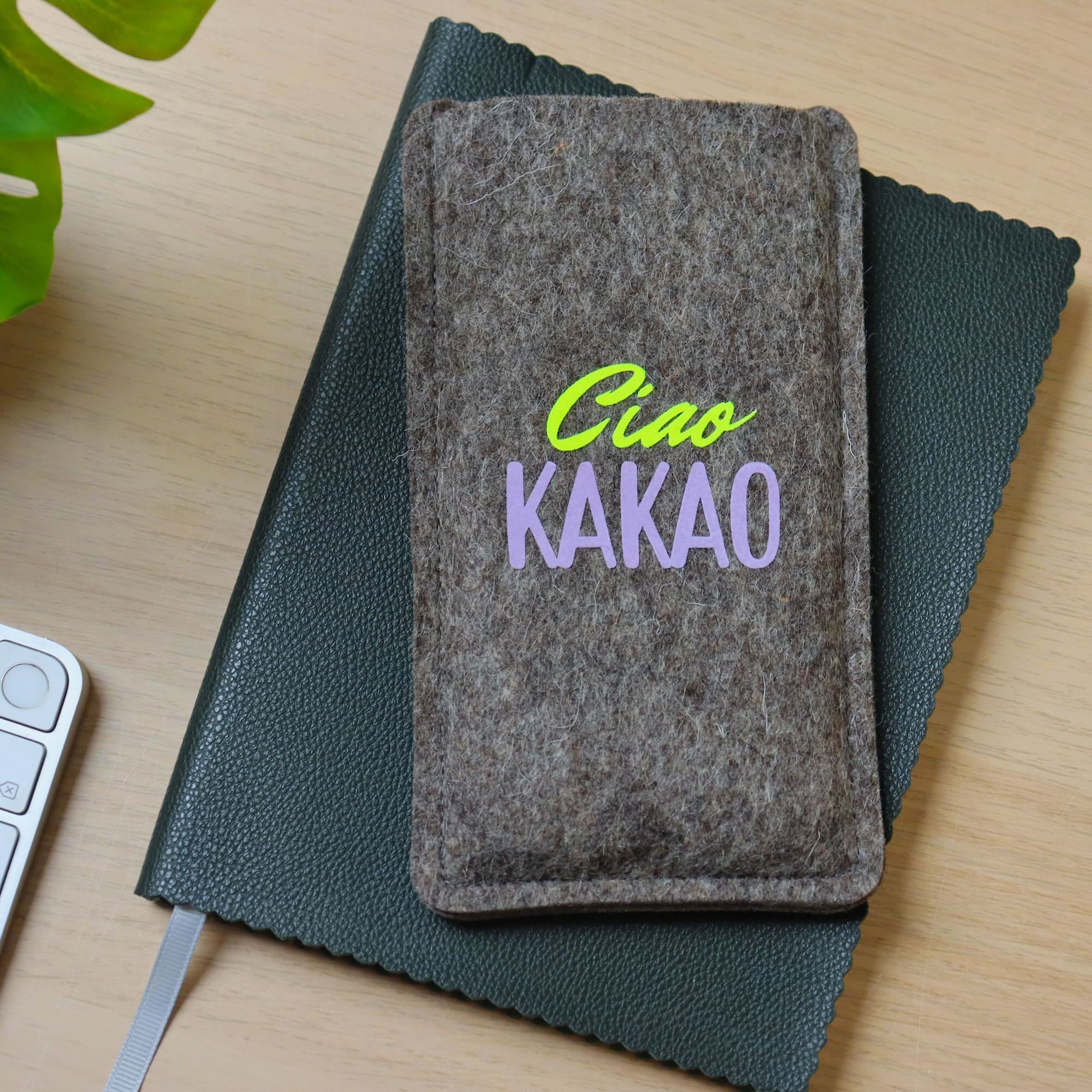 Handytasche aus grauem Filz mit Print "Ciao Kakao", auf einem Notizbuch liegend