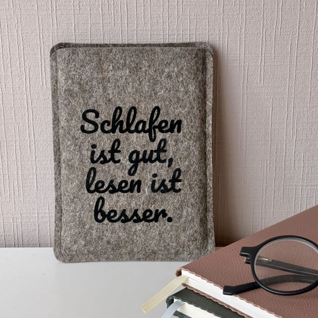 Graue Filzhülle für PocketBook Verse, mit schwarzem Flockprint "Schlafen ist gut, lesen ist besser.", mit Bücherstapel