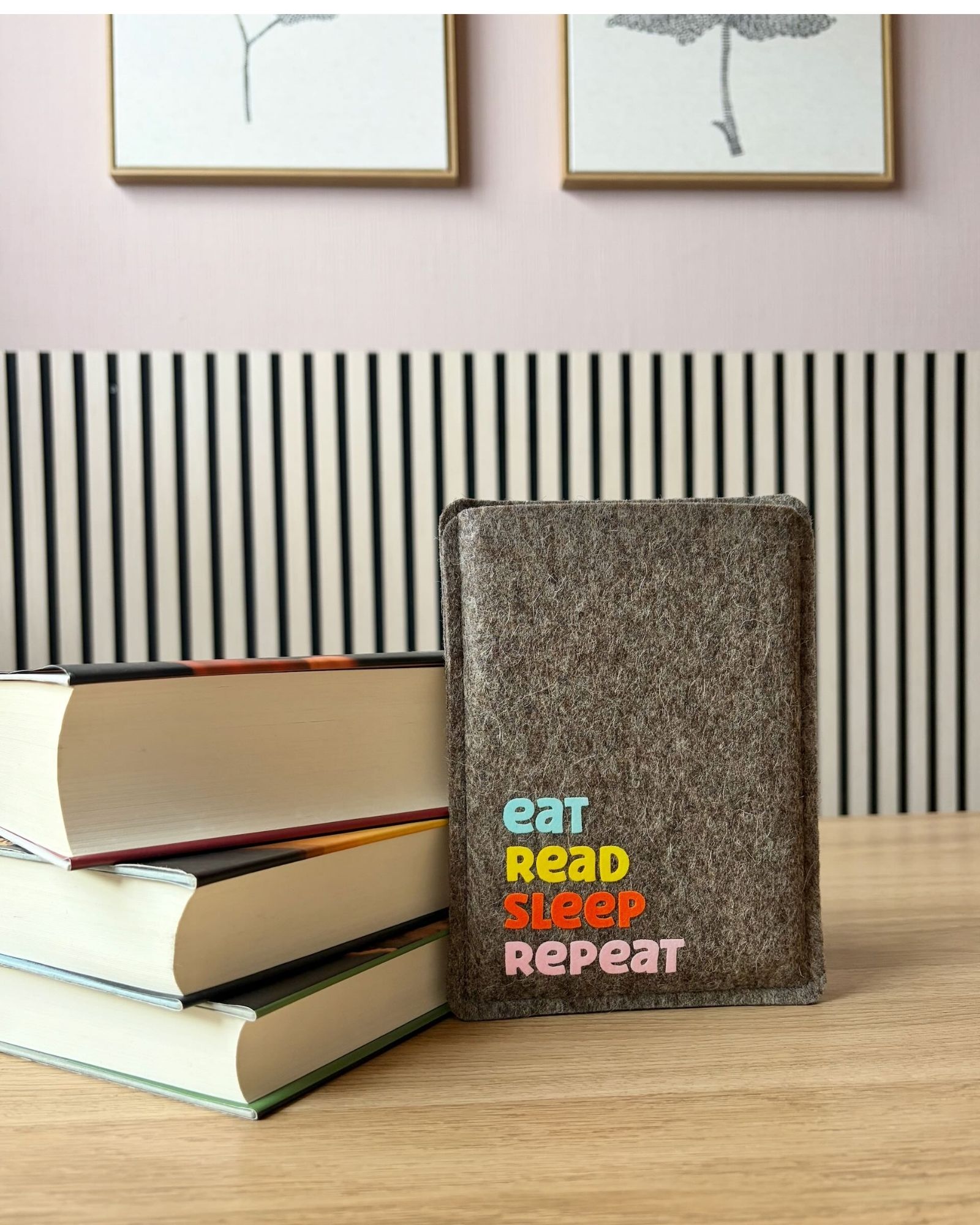eReader Hülle aus grauem Wollfilz, mit buntem Schriftzug "eat read sleep repeat", einfache Einschubhülle für eBook Reader. Die Filzhülle ist an einen Bücherstapel angelehnt.