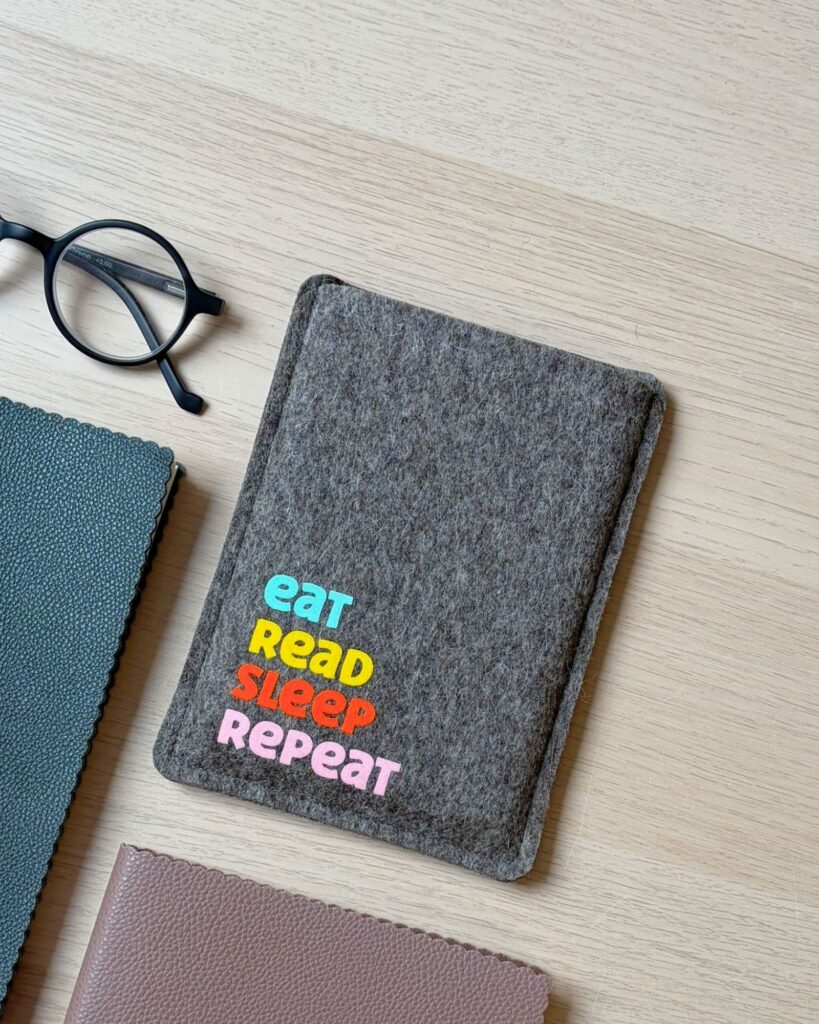 eReader Hülle aus grauem Wollfilz, mit buntem Schriftzug "eat read sleep repeat", einfache Einschubhülle für eBook Reader
