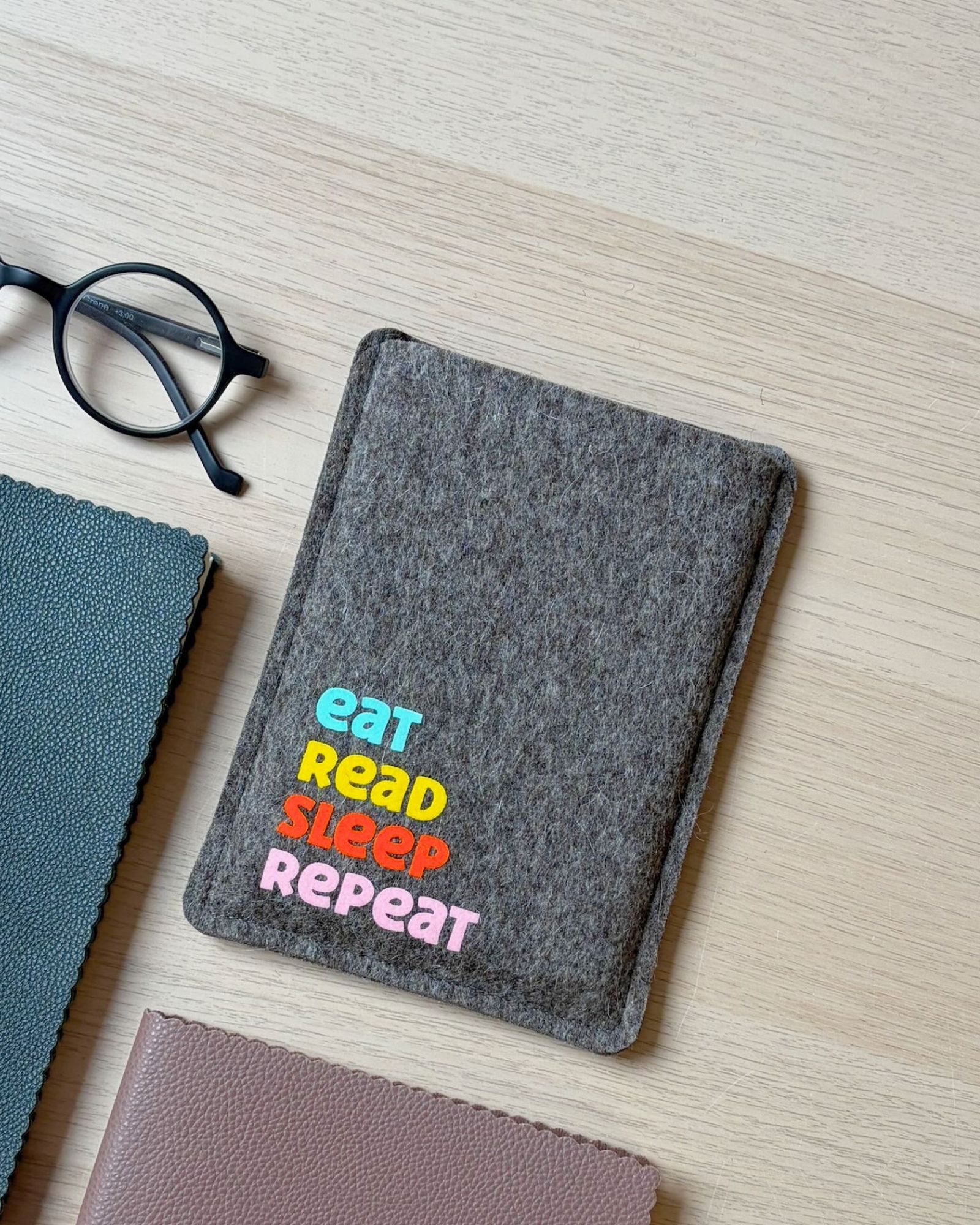 eReader Hülle aus grauem Wollfilz, mit buntem Schriftzug "eat read sleep repeat", einfache Einschubhülle für eBook Reader
